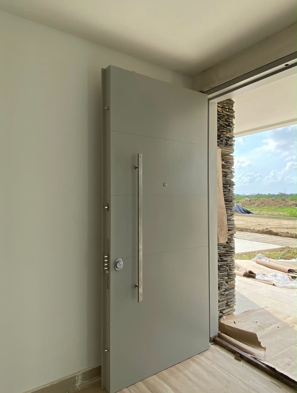 Puerta blindada pivotante de gran formato en gris con manija tubular en acero inoxidable