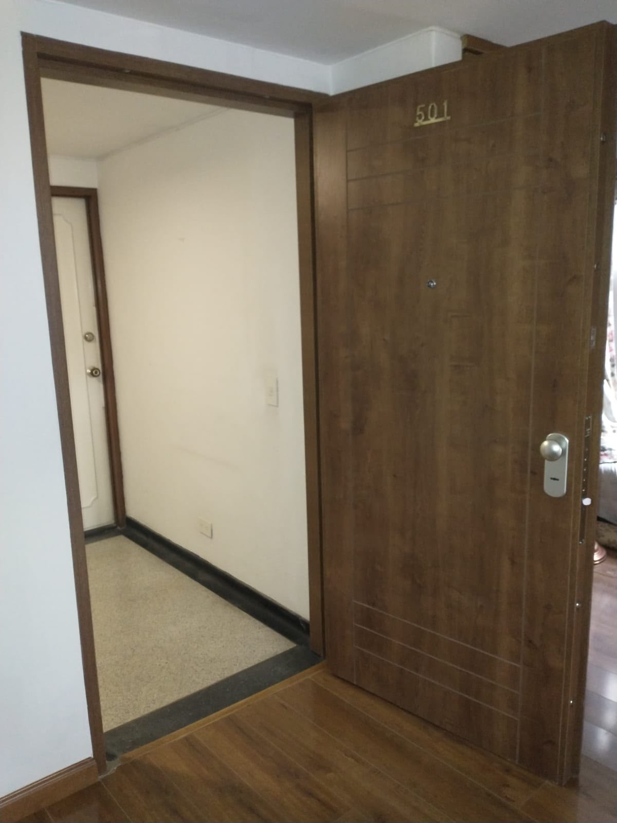 Puerta blindada instalada en apartamento con acabado en madera y número de apartamento en dorado