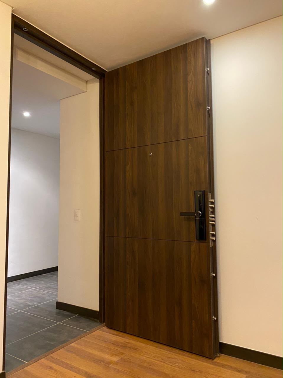 Puerta blindada con acabado en madera nogal oscuro y cerradura digital de manija negra